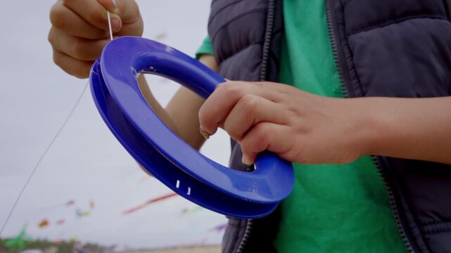 Young child winding kite string on a blue spool outdoors at the beach with focus on hands and playful activity.