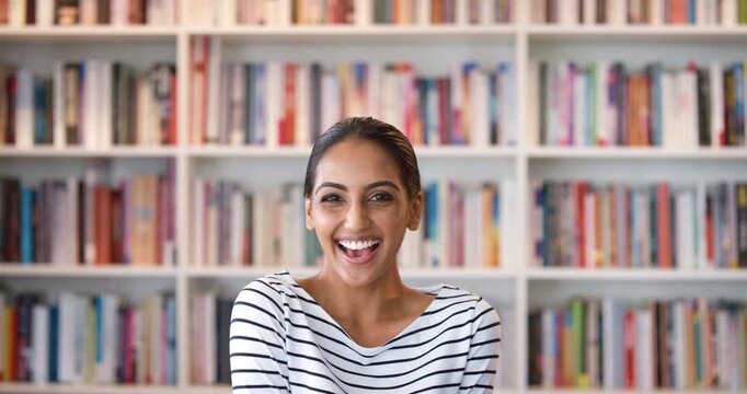 Face, education and Indian woman with laugh in library, university student and learn for scholarship. Portrait, funny person and scholar by bookshelf for learning, knowledge development and smile