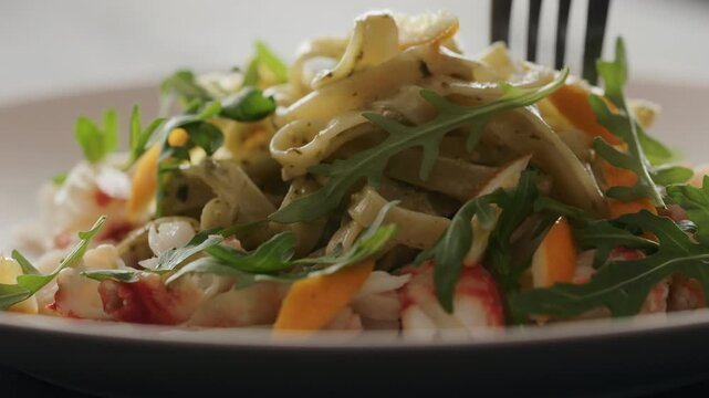 Slow motion eat pesto fettuccine with crab meat on plate closeup