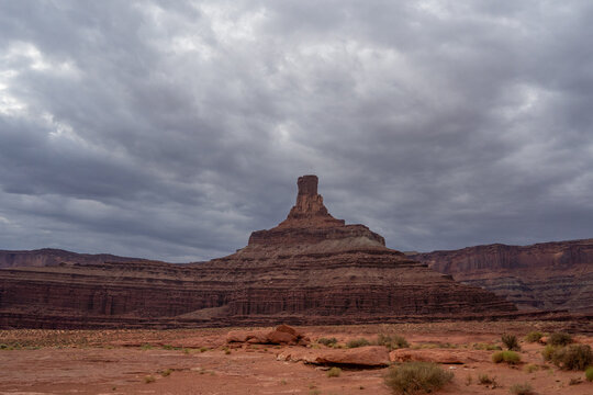 View of a towering red rock butte with layered sandstone formations under a heavy overcast sky in Moab, Utah, United States.