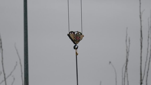 Solitary heartshaped bell hangs softly in gray. Quiet metal ornament dangles amidst overcast winter sky. Peaceful wind chime sways subtly on thin wire near lamppost