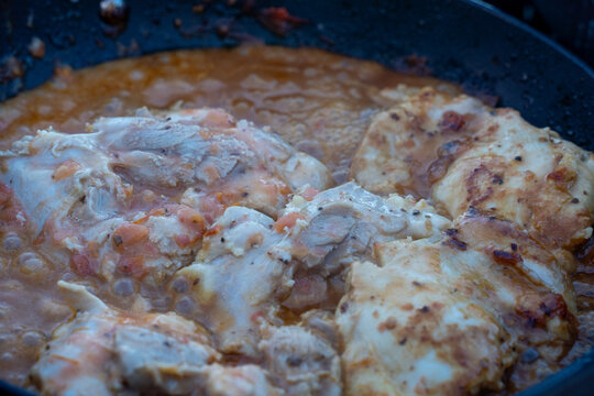 View of chicken pieces simmering in a bubbling tomato sauce inside a dark pan in Moab, Utah, United States.