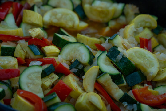View of sliced green and yellow zucchini mixed with red bell peppers and onions cooking in a pan in Moab, Utah, United States.