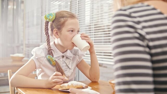 Girl with pigtails eats sweet cakes with her mum in the cafe