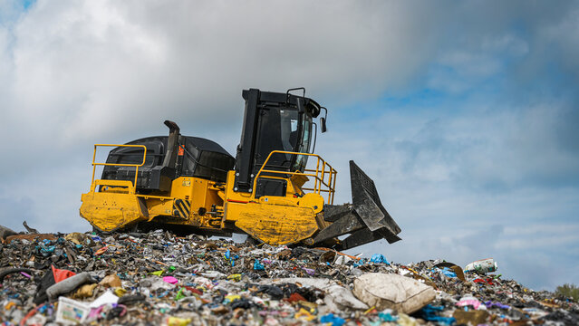 Heavy industrial machinery working at a large landfill site.  A view on a landfill compactor compacting and managing piles of waste.