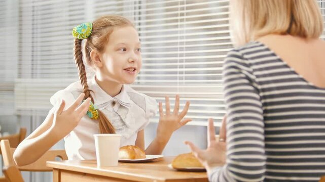 Girl with pigtail is eating sweets in the cafe, talking with her mam and telling a story and gesticulating