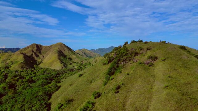 Expansive view of komodo island's rolling hills covered in lush green forest and grasslands under a blue sky. Best aerial view rotation pan to right panorama drone