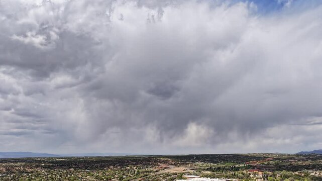 4K drone timelapse captures large rainclouds shifting over western Santa Fe and the arid New Mexico chaparral. Cinematic atmospheric motion reveals high desert shrubland and weather transitions.