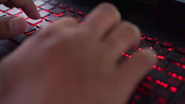 Hand of person typing on laptop keyboard with red LED lights, digital work and tech lifestyle.