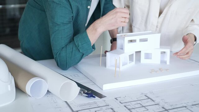 Architects designing house model, reviewing blueprint plans, developing new building project, collaborating on urban construction. Architecture and business concept