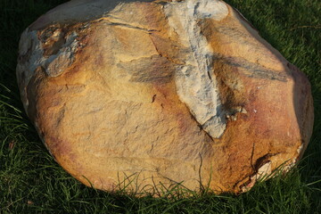 Large, weathered boulder with striking mineral deposits resting on green grass © khomkrit