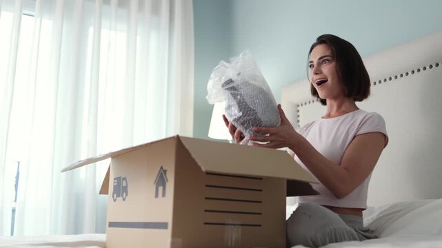 Joyful customer inspecting items from opened parcel at home. Concept online shopping and happiness after delivery.
