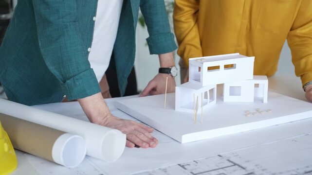 Architects designing residential building structure using scale model and blueprints, planning new construction project. Architecture and business concept