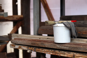 Naklejka premium Painting set: brush, gloves and small white bucket with paint or varnish on wooden background. Workshop. Repair and construction concept. Painting tools on wooden background. Close-up of tools