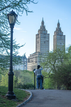 View of Central Park with a woman standing on a path near a street lamp looking at the San Remo towers New York, New York, United States.