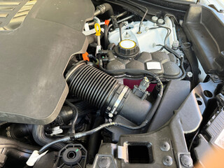 Fototapeta premium Detailed view of automotive engine components including coolant reservoir, intake hose and engine cover inside a modern vehicle. Car maintenance and automotive service concept.