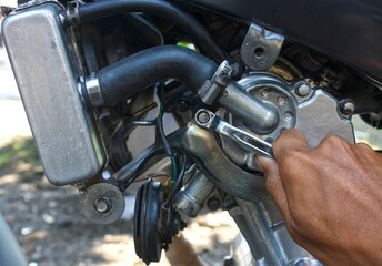 Fototapeta premium Close-up of a mechanic's hand using a wrench to repair a motorcycle engine. Maintenance and DIY repair of a liquid-cooled motorbike. Automotive mechanical workshop concept