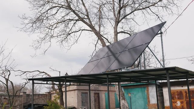 Solar panel array sits on a metal carport structure in a backyard. Bare winter trees and brick buildings frame the scene under soft overcast light. Renewable energy technology for home power