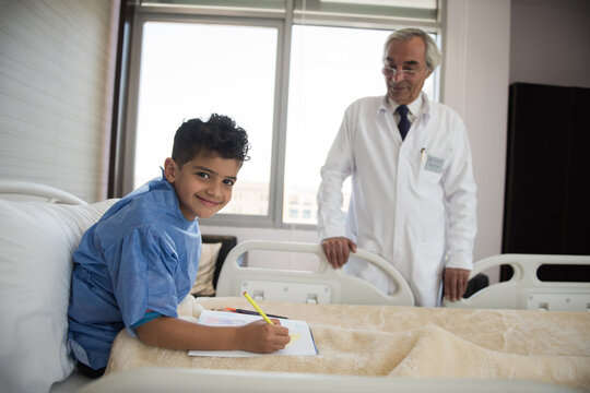 Young Middle Eastern boy patient drawing in eye hospital bed while doctor watches in clinic in Egypt