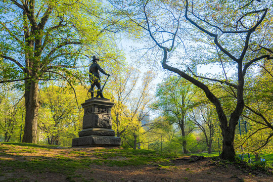 View of The Pilgrim statue surrounded by lush green trees and spring foliage in Central Park New York, New York, United States.
