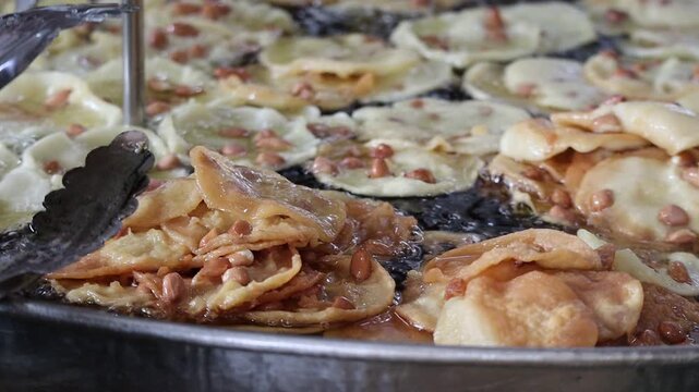 Close-up of traditional Indonesian peanut crackers (Rempeyek) deep-frying in a large vat of hot oil at a Thai street market.