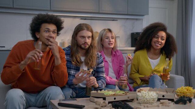 Amazed four multiethnic friends men women watching TV sport game home couch eating pizza together Caucasian girls African American guys excited fans friendship weekend watch television program indoors