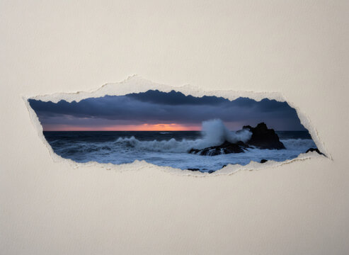 Ocean waves crashing against rocks at sunset seen through a hole ripped in white paper. Concept of discovery, breaking through barriers and travel adventure. Surreal nature window frame.