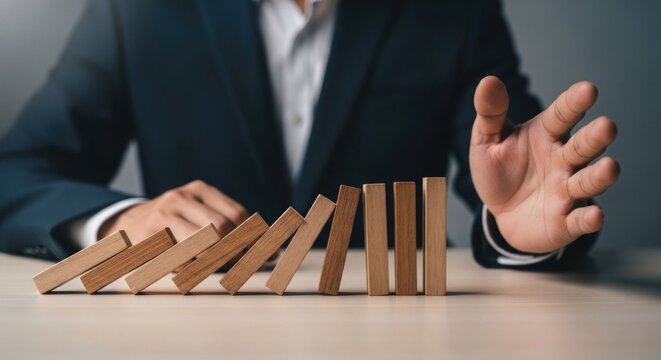 Businessman stopping domino effect to prevent crisis.