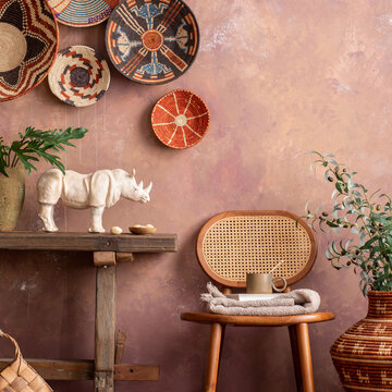 The stylish ethnic compostion at living room interior with wicker baskets, wooden bench, rattan chair and elegant personal accessories. Cozy apartment. Home decor. Template.