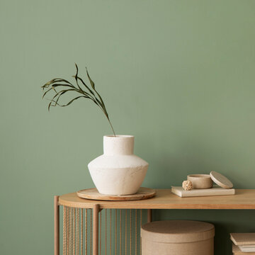 Stylish living room interior design wooden chest of drawers, beige vase and creative home accessories. Sage green wall. Copy space. Template.