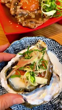  Close-up of a hand holding a fresh oyster in shell with colorful Japanese garnishes