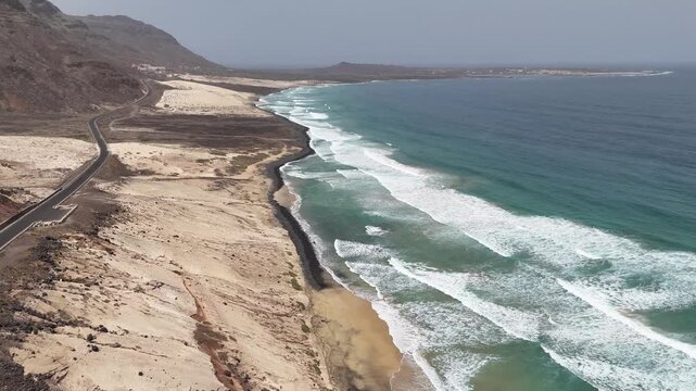 Dramatic aerial perspective of the intersection between desert dunes and the ocean at Praia Grande, Sao Vicente, drone view of the unique geological formations in Cabo Verde.