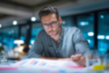 Obraz premium Blurred Focused Businessman Working Late in Modern Office, Analyzing Charts and Graphs