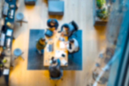 Blurred Diverse team collaborating around wooden conference table in modern office space