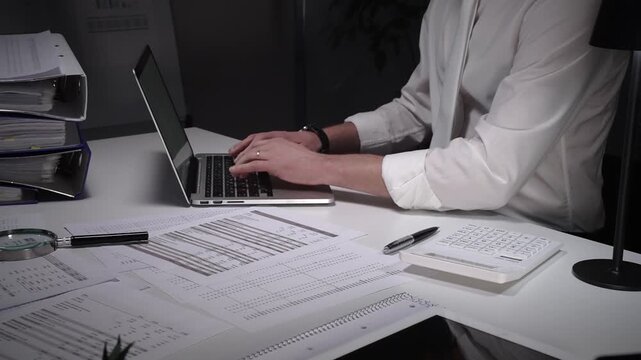 Dedicated finance professional at a cluttered desk, focused on analyzing documents and numbers with laptop, calculator and magnifying glass while managing company records and budgets