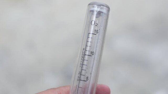 A hand holds an oxygen flow meter tube against a blurred background, showcasing the clear 'O2' labeling and measurement markings on this essential medical device.
