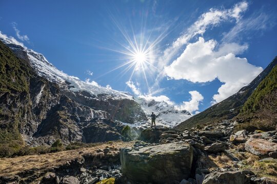 Mountaineer stands on rocks, view of Rob Roy Glacier, Sun Star, Mount Aspiring National Park, Otago, South Island, New Zealand