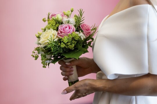 Bride holding bridal bouquet with roses in front of pink wall