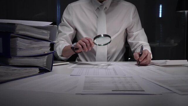 Professional businessman using a magnifying glass discovering financial data and scrutinizing corporate tax documents. Auditing company records for fraud and errors