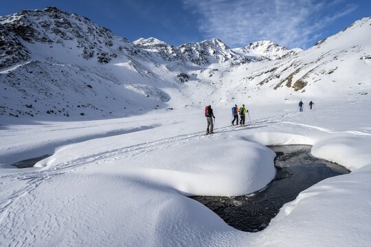 Small stream in a snow-covered mountain landscape, ski tourers in a valley, ascent to the Madritschspitze, Ortler Alps, Vinschgau, Italy