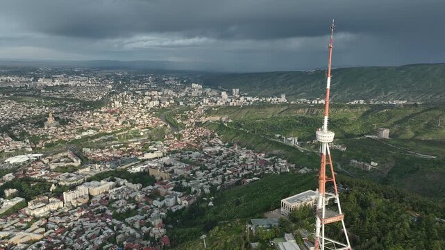 Aerial view of the Funicular Restaurant at Mtatsminda Park during sunset. Dynamic drone shot of a TV tower with Tbilisi city in the background.
