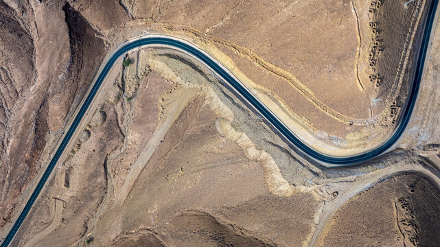 Top view aerial drone shot of winding S-curve mountain road through arid desert terrain, Morocco
