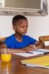 African American child boy in blue tee studying at dining table with notebook pencil orange juice © wavebreak3