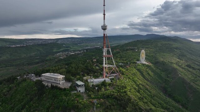 Aerial view of the Funicular Restaurant at Mtatsminda Park during sunset. Dynamic drone shot of a TV tower with Tbilisi city in the background.