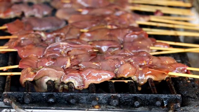 Close-up of marinated chicken livers on skewers grilling over charcoal on a street food BBQ grill.