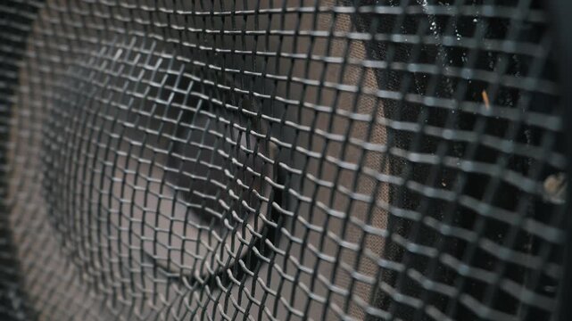 A close-up macro of a black metal speaker grille vibrating as the internal acoustic cone pumps to heavy bass. Concept of loud sound systems, electronic music energy, and powerful acoustics.