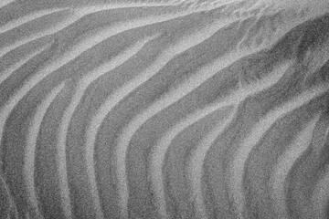 Black and white close-up photograph of wind-shaped sand dunes with soft ripples and natural patterns. The image highlights texture, curves, and minimal abstract forms, ideal for nature, desert, geolog © Erik
