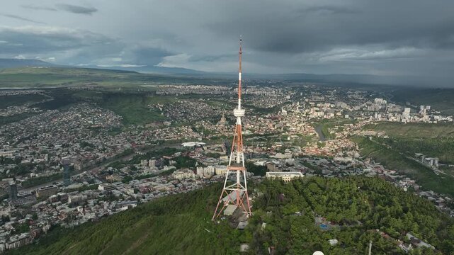 Aerial view of the Funicular Restaurant at Mtatsminda Park during sunset. Dynamic drone shot of a TV tower with Tbilisi city in the background.