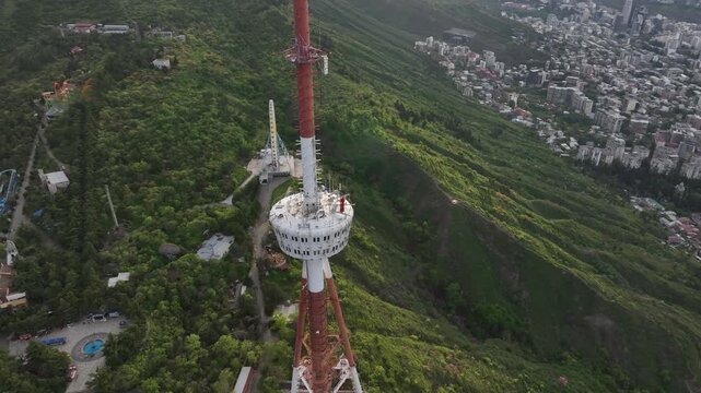 Aerial view of the Funicular Restaurant at Mtatsminda Park during sunset. Dynamic drone shot of a TV tower with Tbilisi city in the background.