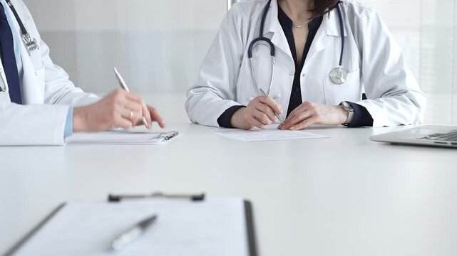 Medical professionals in lab coats writing notes during clinical consultation at modern healthcare office. Medical team meeting